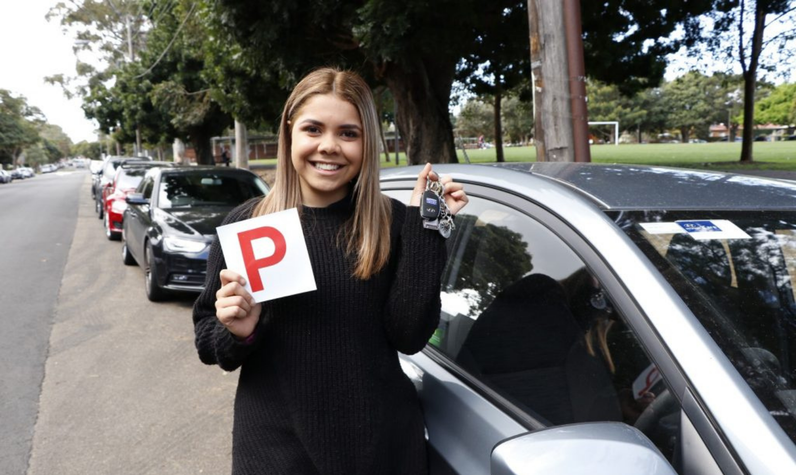 Young person holds up car keys and a 'P' plate