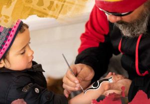 Cover of Reconciliation Australia Annual Review 2018-2019. Image shows a man painting an Aboriginal design on a young girl's arm.