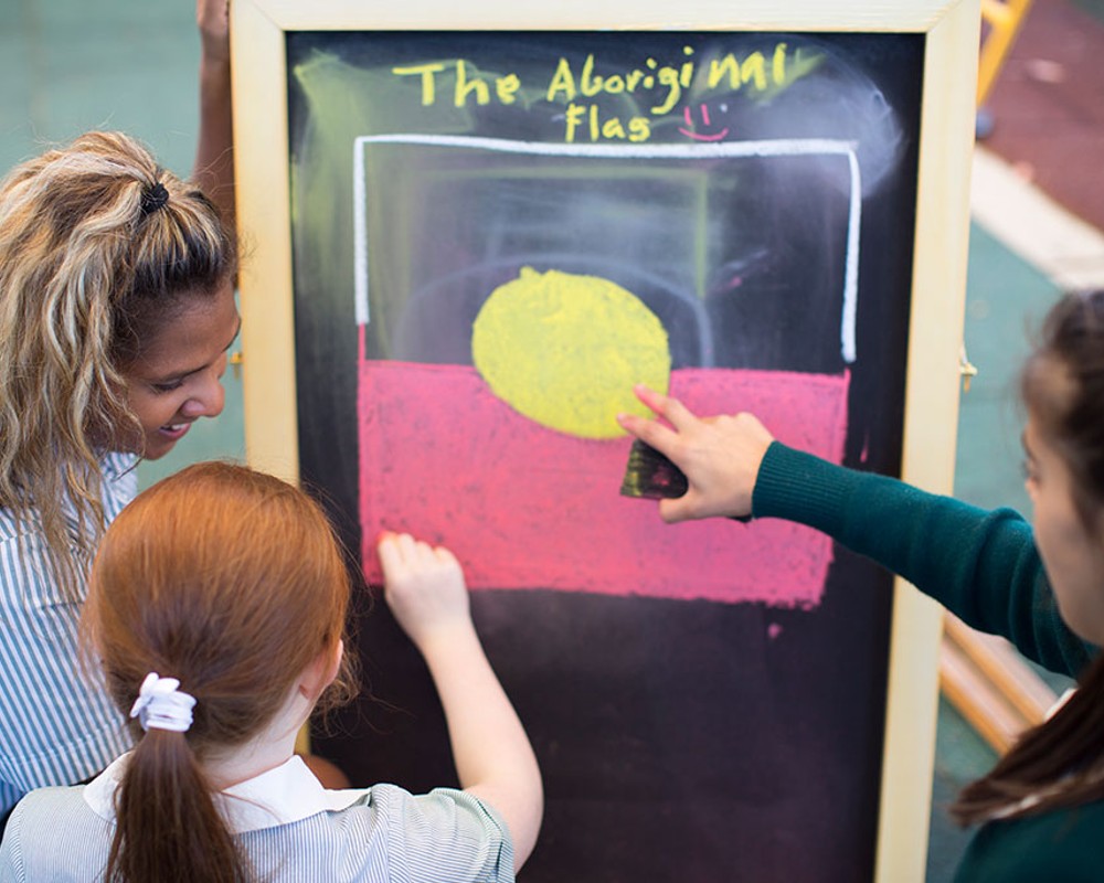 Three school children looking at and talking about the Aboriginal Flag