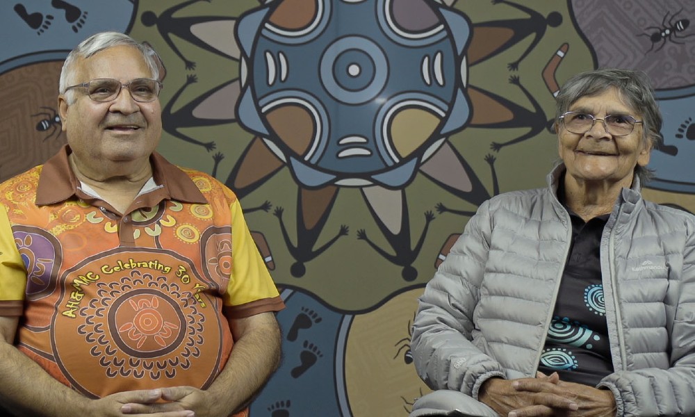 H&MRC HREC Community Representatives, Uncle Danny Kelly and Aunty Rochelle Patten, sitting in front of the ethics committee’s 25th anniversary artwork by Aunty Rochelle.