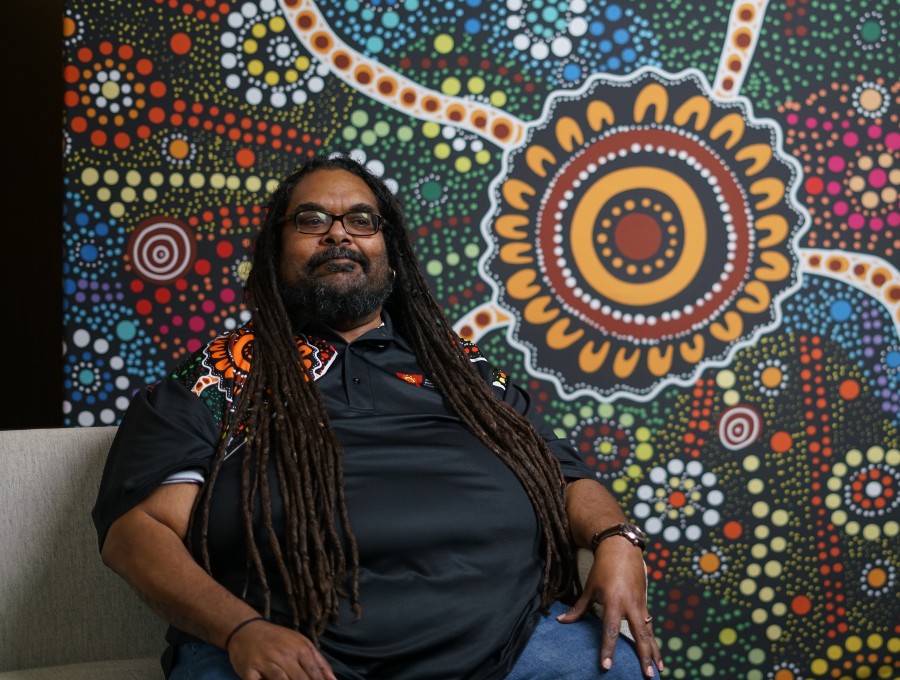 A person sits in front of a large Aboriginal artwork