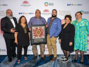 Representatives of Brewerrina Local Aboriginal Land Council stand smiling and holding their award with Reconciliation Australia CEO Karen Muindine.