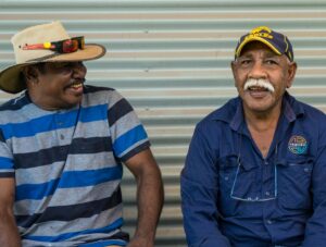 Two men sit side by side smiling