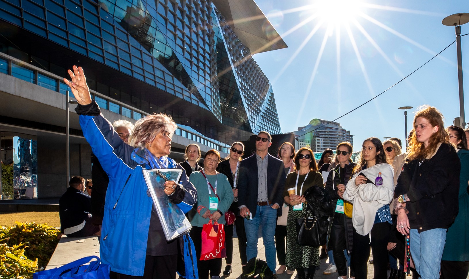 Woman talking to a group of people outside in the sun. She is describing the history of a a location to them.