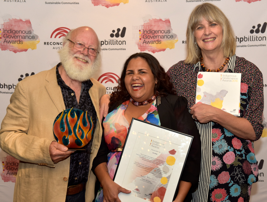 Two women and a man pose for a photo holding their framed award certificate