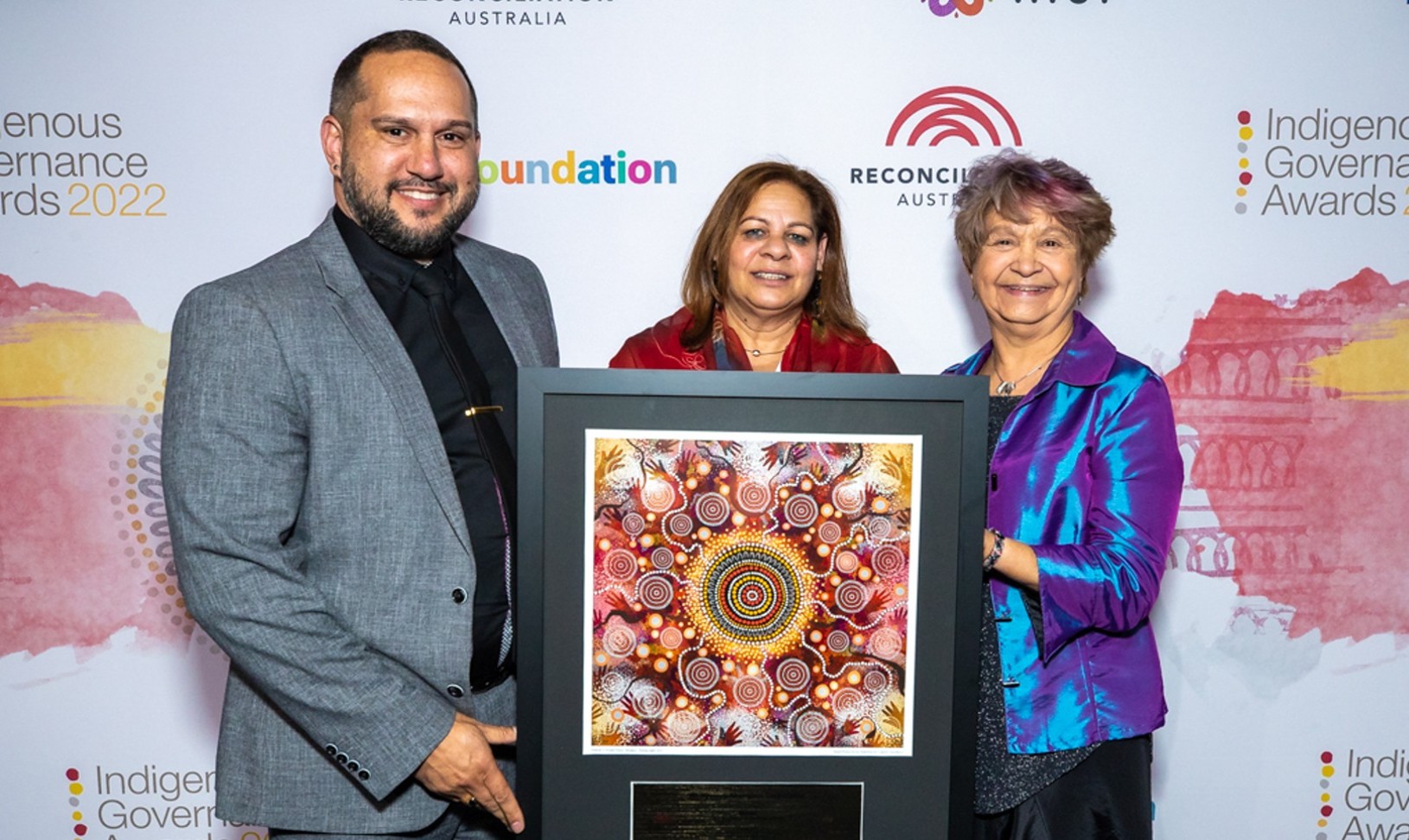 A man and two women in front of a banner holding an Indigenous Governance Award