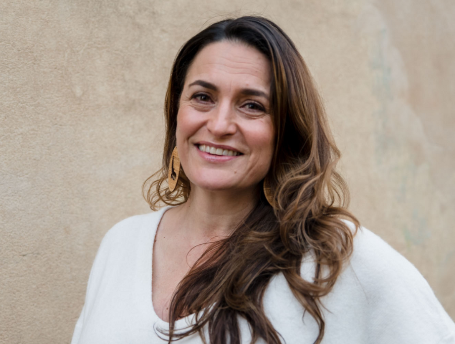 Belinda Duarte wearing a white top and standing in front of a yellow wall.