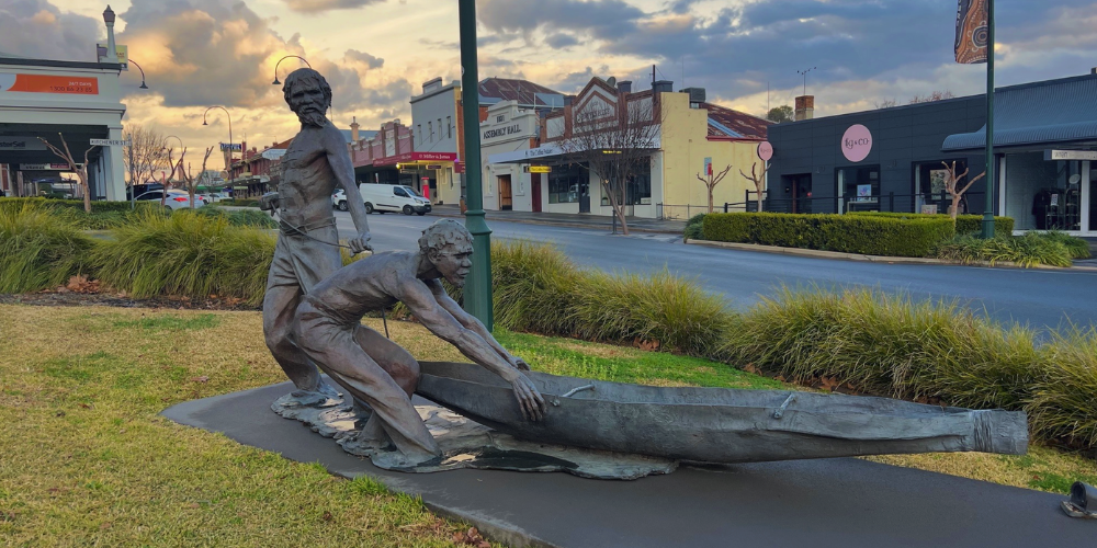 A bronze sculpture of two Aboriginal men pushing out a canoe.