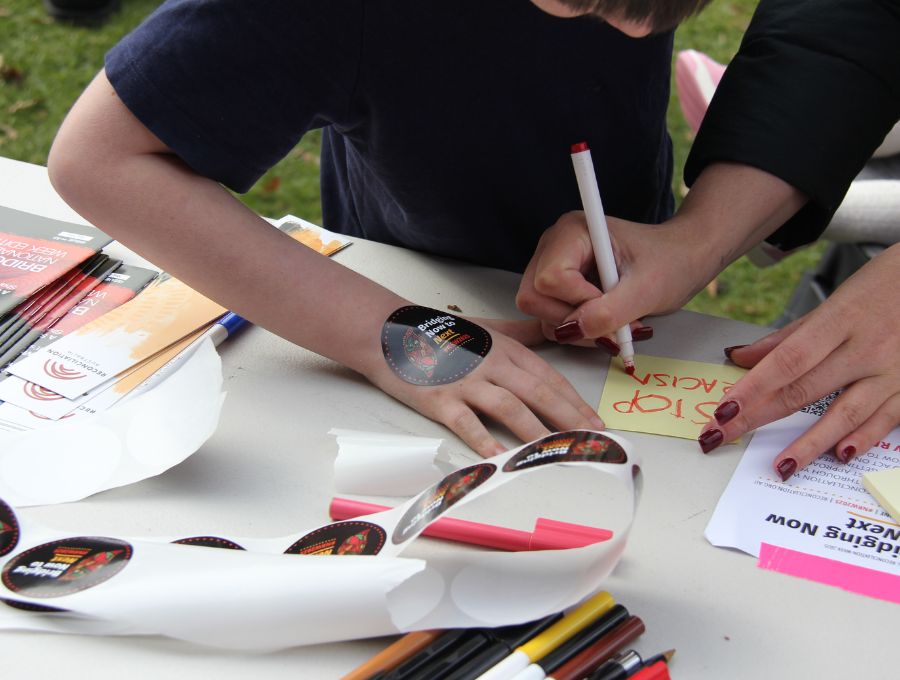A child with a National Reconciliation Week sticker on their hand writes something on post-it note with help from an adult.