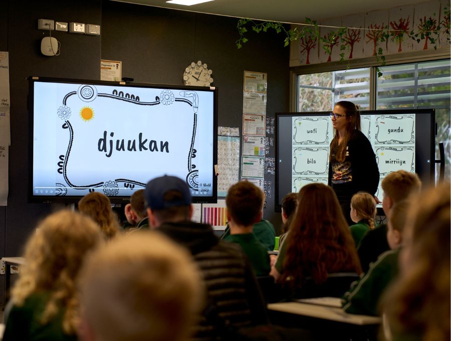 A group of students sit in front of a screen with the word 'djuukan' on it.