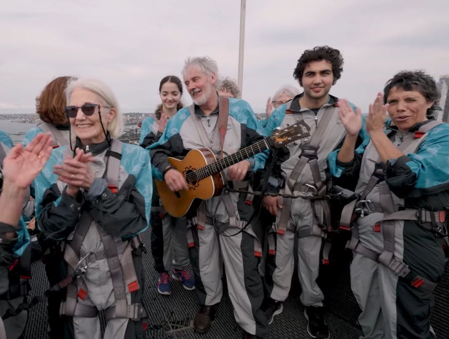 A group of people singing, standing atop the Sydney Harbour Bridge.