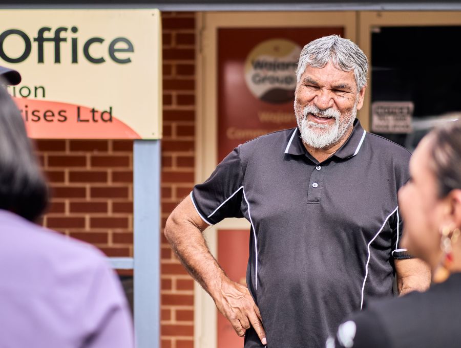 An Elder stands with his hands on his hips in front of an office, smiling.