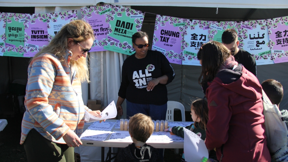 A crowd of people at a National Reconciliation Week 2026 event; standing in the sun in front of a stall.