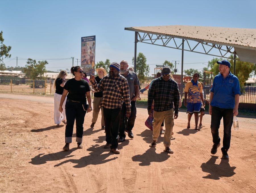 A group of people, Indigenous and non-Indigenous, walking together in an outback community.