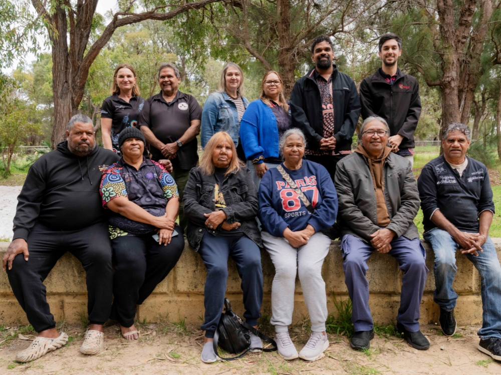 Group of people - front row sitting on low stone wall, back row standing behind.